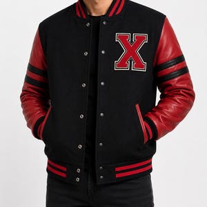 Könnte beinhalten: Eine schwarze Collegejacke mit roten Lederärmeln und einem großen, roten Buchstaben X als Aufnäher auf der linken Brust. Die Jacke verfügt über einen schwarzen Rippstrickkragen, Bündchen und einen Saum mit roten Streifen.
