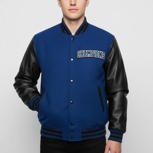 May include: Blue varsity jacket with black leather sleeves. The jacket features the word "CHAMPIONS" on the chest. The jacket has a black and white striped collar, cuffs, and hem. The jacket has a button-up front.
