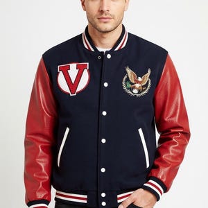 May include: Navy blue varsity jacket with red leather sleeves. The jacket features a large white and red "V" patch and an embroidered eagle emblem. White stripes accent the collar, cuffs, and hem. The jacket has a button-up front.