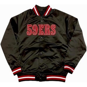Puede incluir: Chaqueta bomber de satén negro con el texto "59ERS" en escritura roja en el pecho. La chaqueta tiene cuello, puños y dobladillo acanalados con rayas rojas y blancas. La chaqueta tiene cierre de botones.
