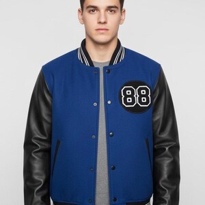 May include: A blue varsity jacket with black leather sleeves. The jacket features a black and white patch with the number "88" on the chest. The collar and cuffs have white stripes. The jacket has a button-up front.