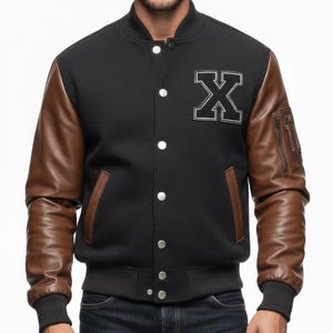 May include: Black varsity jacket with brown leather sleeves. The jacket features a white embroidered "X" patch on the chest, a ribbed collar, cuffs, and hem, and a zippered pocket on the left sleeve. The jacket has a button-up front.