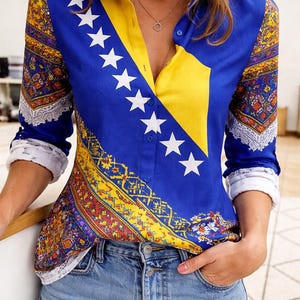 May include: A blue button-down shirt with a yellow panel and white stars, featuring a decorative pattern on the sleeves. The shirt is paired with blue jeans.