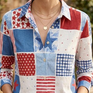 Op de afbeelding: Een patchwork overhemd in rood, wit en blauw, met ster- en streepmotieven. Het shirt met lange mouwen wordt gecombineerd met een blauwe jeans. Het model draagt gouden kettingen en een armband.