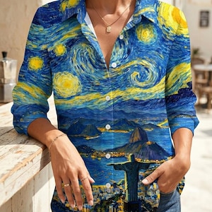 May include: A button-down shirt featuring a vibrant print inspired by Van Gogh's "Starry Night" and a cityscape. The long-sleeved shirt has a blue and yellow color scheme, with a white collar and buttons. The shirt is paired with blue jeans.