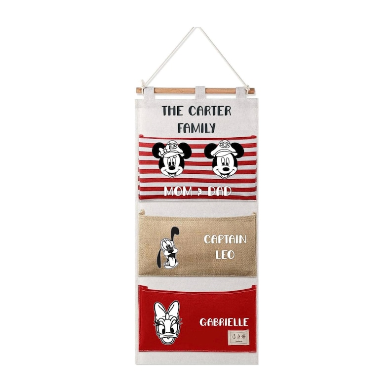 May include: A hanging wall organizer with three pockets featuring the text THE CARTER FAMILY. The top pocket has red and white stripes with two mouse characters and the text MOM & DAD. The middle pocket is tan with a dog graphic and CAPTAIN LEO.