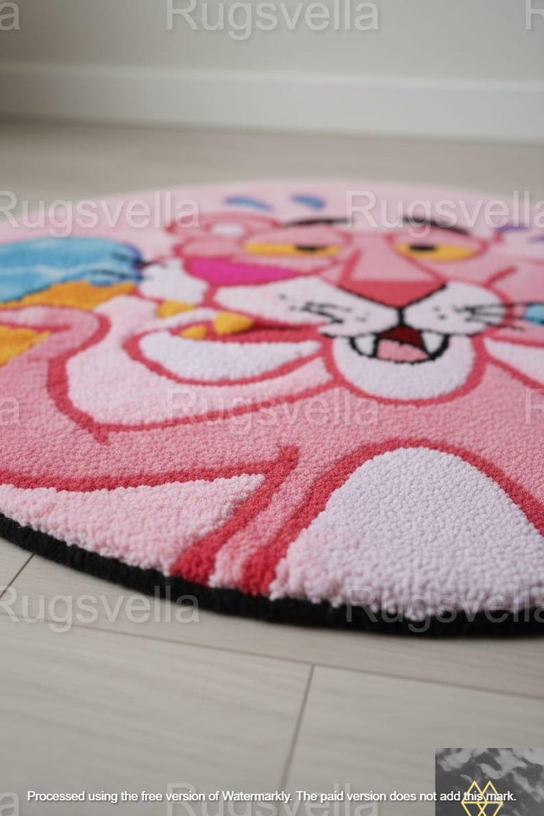 Op de afbeelding: Een ronde, roze vloerkleed met een cartoonontwerp van de Roze Panter. Het vloerkleed heeft een zwarte rand en is gemaakt van een zacht, getextureerd materiaal. De Roze Panter wordt afgebeeld met een glimlachende uitdrukking.