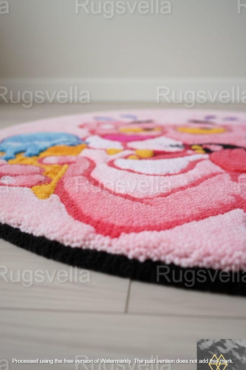 Op de afbeelding: Een ronde, roze vloerkleed met een cartoon-personage ontwerp. Het kleed heeft een zwarte rand en een getextureerd oppervlak. Het ontwerp bevat roze, gele en blauwe tinten. Geschikt voor een kinderkamer.