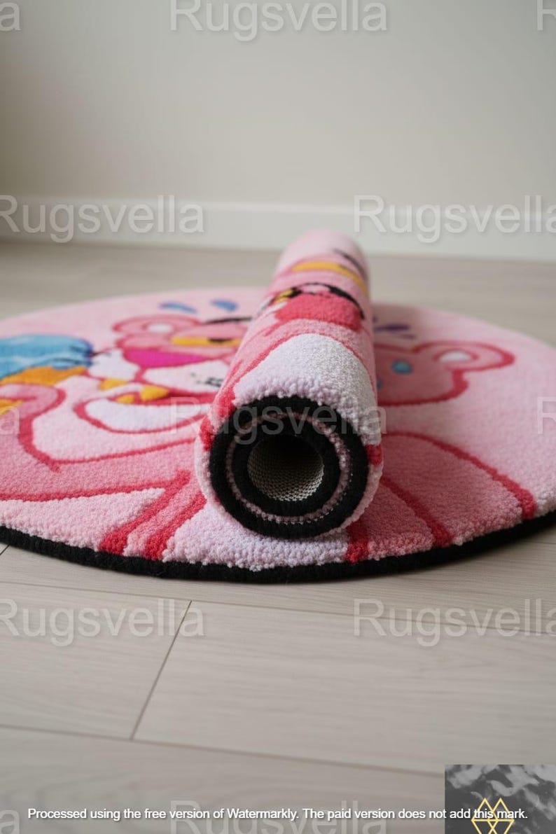 Op de afbeelding: Een ronde roze vloerkleed met het stripfiguur Pink Panther, gedeeltelijk opgerold. Het kleed heeft een zwarte rand en een getextureerd oppervlak. Het ontwerp bevat roze, rode en blauwe tinten.