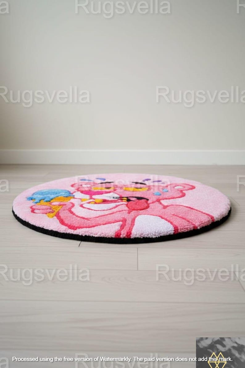 Op de afbeelding: Een ronde roze vloerkleed met het stripfiguur Pink Panther die een ijsje vasthoudt. Het vloerkleed heeft een zwarte rand en ligt op een lichte houten vloer. De Pink Panther is in roze en rode tinten.