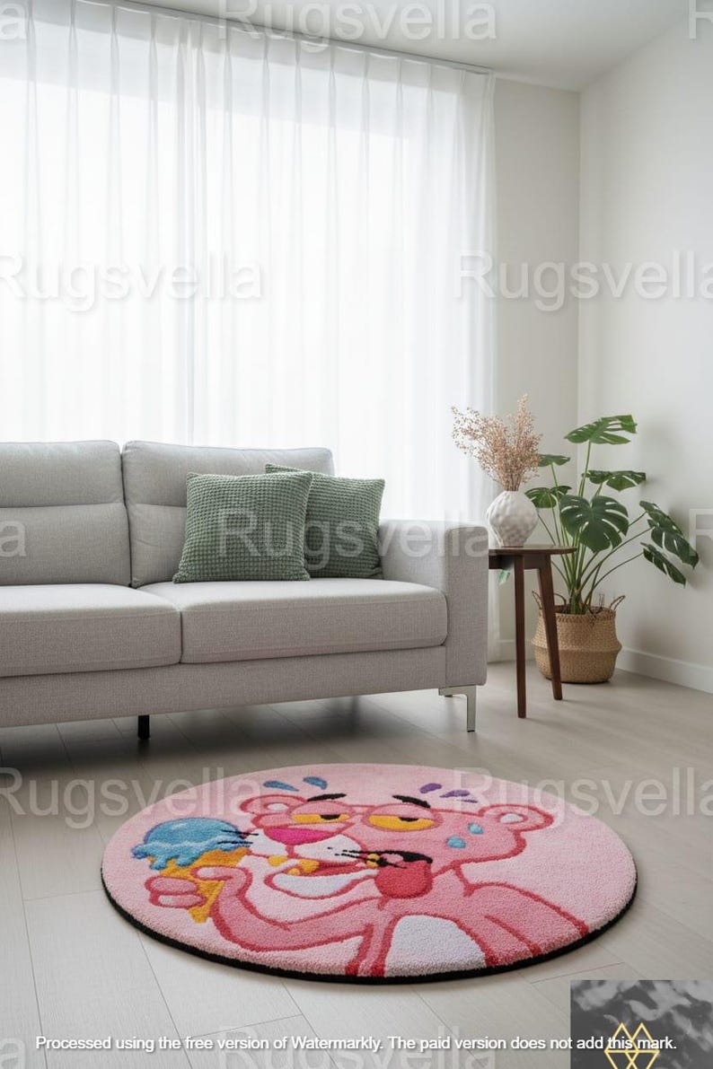 Op de afbeelding: Een ronde roze vloerkleed met een cartoon Pink Panther die een ijsje vasthoudt. Het kleed heeft een zwarte rand en ligt op een lichte houten vloer. De achtergrond toont een grijze bank, groene kussens en een plant in een pot.