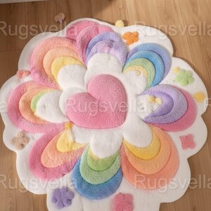 May include: A colorful, flower-shaped rug with a heart-shaped center. The rug features a rainbow design with shades of pink, yellow, green, and blue. Small, flower-shaped accents are scattered around the edges. The rug is made of a soft, plush material.