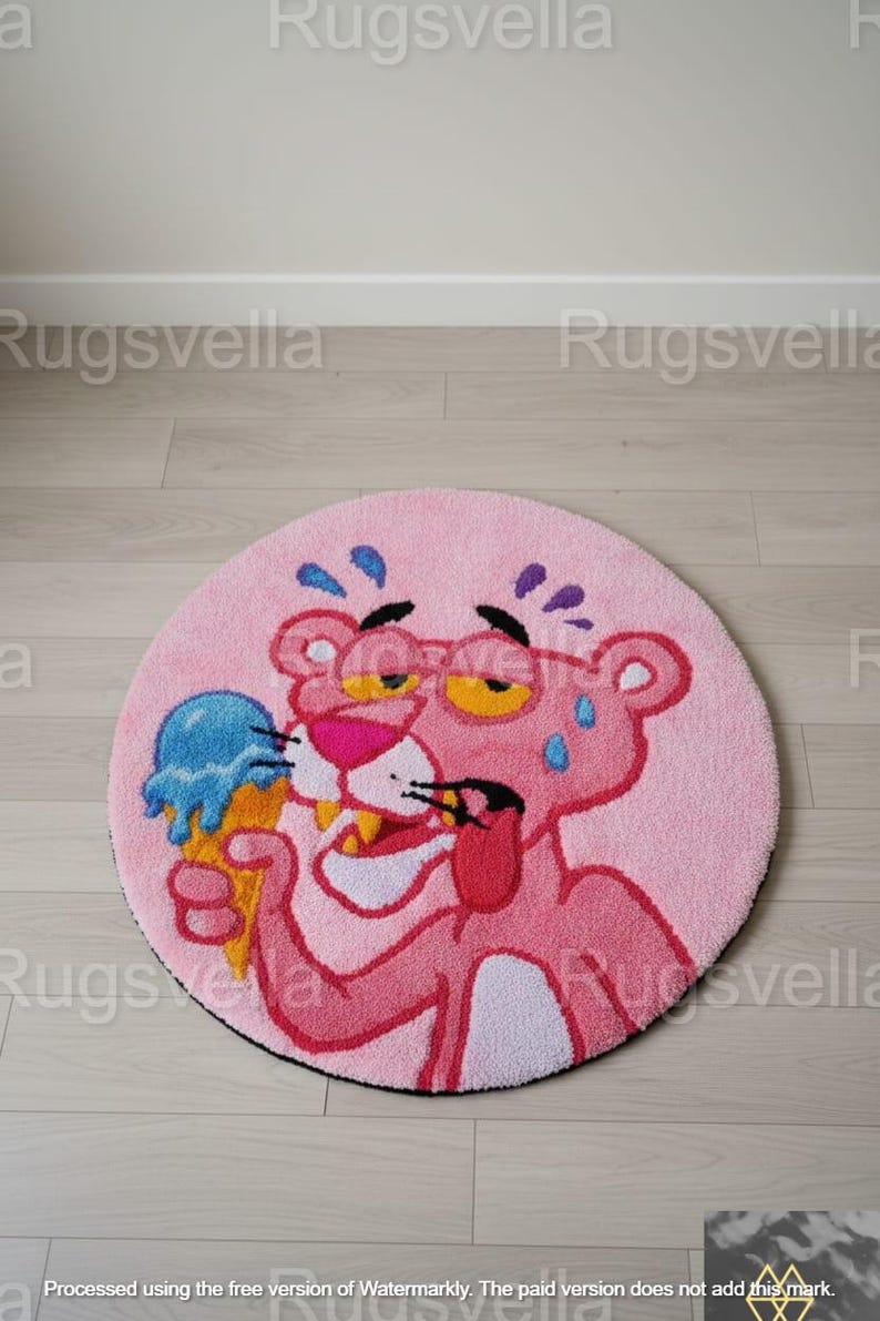Op de afbeelding: Een ronde roze vloerkleed met een cartoon Pink Panther-personage met een bril en een blauw ijsje. Het vloerkleed heeft een zwarte rand en ligt op een lichte houten vloer. De diameter van het vloerkleed is ongeveer 100 cm.