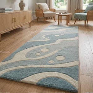 Könnte beinhalten: Ein rechteckiger Teppich mit einem abstrakten Design in Blau, Hellblau und Off-White. Der Teppich hat ein wellenförmiges Muster mit kreisförmigen Akzenten, das einen modernen und strukturierten Look erzeugt. Der Teppich liegt auf einem Holzboden.