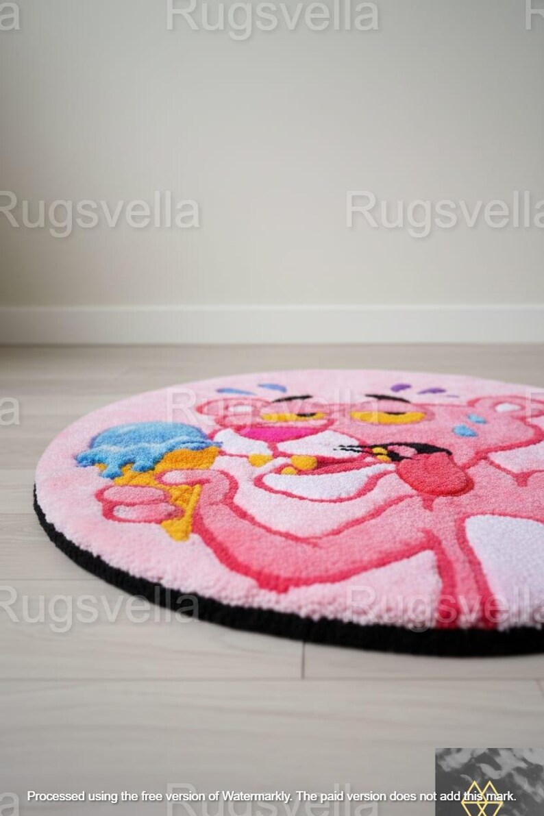 Op de afbeelding: Een ronde roze vloerkleed met de tekenfilmfiguur Pink Panther die een blauw ijsje vasthoudt. Het vloerkleed heeft een zwarte rand en ligt op een lichte houten vloer. Het woord "Rugsvella" staat als watermerk op de afbeelding.