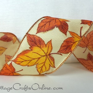 May include: A cream-colored ribbon with a gold metallic edge features a repeating pattern of orange and yellow autumn leaves. The ribbon is perfect for fall crafts and decorations.