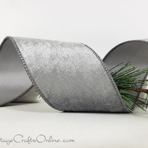 May include: A wide, metallic silver ribbon with a textured, shimmering finish and stitched edges, arranged in a loose, flowing wave pattern. A small, green artificial pine needle sprig is tucked behind the ribbon. The text CottageCraftsOnline.com is visible.