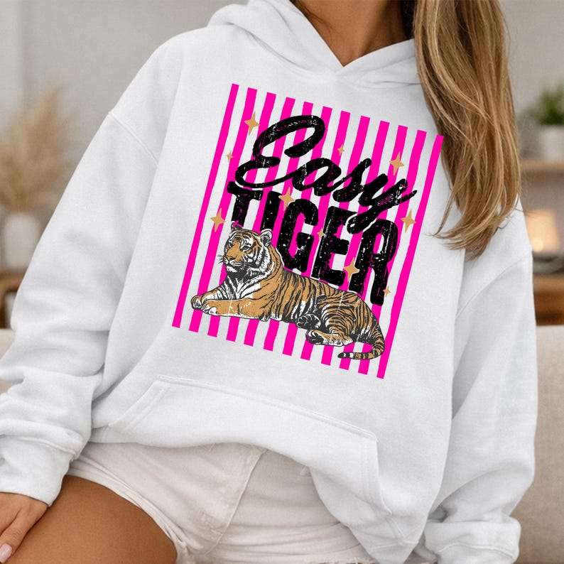 Pu&ograve; includere: Felpa con cappuccio bianca con una grafica frontale raffigurante un'illustrazione di tigre e la scritta "Easy Tiger" in nero. La grafica &egrave; ambientata su uno sfondo a righe rosa e bianche con stelle dorate. La felpa ha una tasca a marsupio.