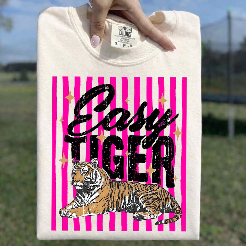Pu&ograve; includere: Felpa color crema con un design grafico. Il design presenta le parole "Easy Tiger" in nero, su uno sfondo a righe rosa. Un'illustrazione di tigre &egrave; sotto il testo, con accenti di stelle dorate.