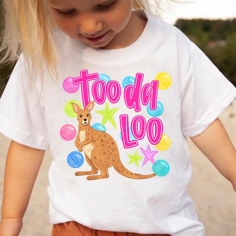 K&ouml;nnte beinhalten: Wei&szlig;es T-Shirt mit einem Cartoon-K&auml;nguru und dem pinkfarbenen Text "Tooda Loo". Das Design umfasst bunte Sterne und Blasenakzente. Das K&auml;nguru ist braun mit einem hellbraunen Bauch.