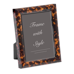 May include: A rectangular picture frame with a tortoiseshell pattern. The frame has a dark brown and amber color scheme. The text "Frame with Style" is displayed in white script on a gray background.