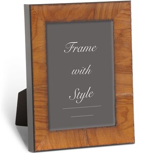 May include: A rectangular wooden picture frame with a dark gray interior. The frame has a light brown, textured finish. The text "Frame with Style" is written in white script. The frame is propped up with a black easel back.