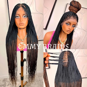 May include: A black and brown braided wig on a mannequin head. The wig features long, individual braids. The text "EMMY BRAIDS" is visible. The wig is shown in various styles, including a bun. Braids are a popular hairstyle.
