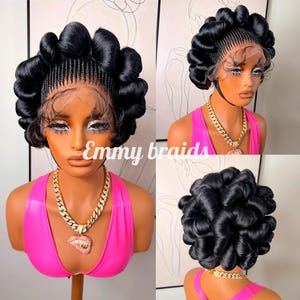 May include: A black braided wig with a lace front, styled with voluminous, rolled sections. The wig is displayed on a mannequin wearing a pink top and a gold chain necklace with a pendant. The text "Emmy braids" is visible.