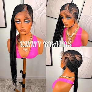 May include: A black braided wig with a side parting and long braids. The wig is displayed on a mannequin head wearing a pink top and gold chain necklace. The text "EMMY BRAIDS" is visible.