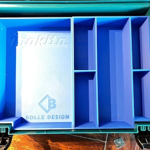 Peut inclure: Un organisateur d'outils bleu sarcelle et bleu avec plusieurs compartiments. L'organisateur a un intérieur bleu avec le logo "Makita" et le texte "BOLLE DESIGN". Les compartiments sont de tailles et de formes variées, conçus pour le rangement des outils.