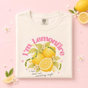 May include: Cream-colored t-shirt with a graphic design featuring lemons and the text "Lemonfire." The design includes the phrases "I'm impulsive," "says what she thinks," and "I turn chaos into somethings bright."