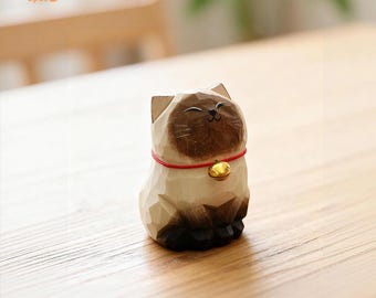 May include: A wooden cat figurine with a red collar and a gold bell. The cat has a light brown face and ears, with a darker brown nose and eyes. The figurine is sitting on a wooden surface. The logo "Curve Spot" is in the top left corner.