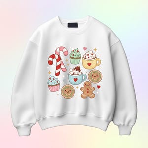May include: White sweatshirt featuring a colorful Christmas-themed design. The graphic includes a candy cane, cupcakes, mugs of hot chocolate, gingerbread cookies, and other festive elements. The design is in a cartoon style with bright colors and heart accents.
