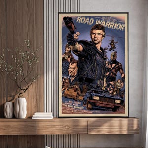 May include: Framed movie poster for "Road Warrior" featuring Mel Gibson. The poster has a blue background with action scenes, including a car, helicopter, and characters with weapons. The title is at the top.