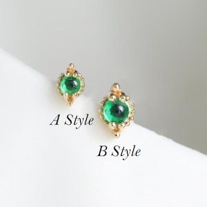 May include: Two gold stud earrings featuring round green gemstones. The earring labeled A Style has a smaller, pointed setting, while the earring labeled B Style has a slightly larger, more rounded setting with decorative beaded metal accents.