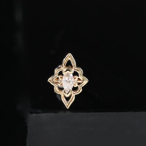 May include: A gold stud earring featuring a marquise-cut clear gemstone at the centre, surrounded by an intricate, symmetrical, four-pointed star-shaped metal frame with openwork detailing, creating a delicate and ornate appearance.