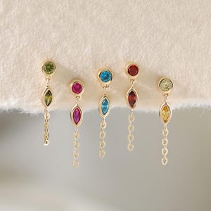 May include: Five gold earrings, each featuring a small round gemstone at the top and a marquise-cut gemstone below, connected by a short gold chain. The earrings display various gemstone colors including green, pink, blue, red, and yellow.