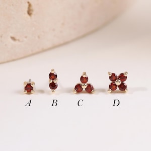 Può includere: Quattro orecchini a lobo in oro con pietre preziose granato rosso scuro. L'opzione A è una pietra singola, B ne ha due, C ne ha tre in un grappolo triangolare e D ne ha quattro a forma di fiore. Ogni pezzo è contrassegnato con le lettere A, B, C e D.