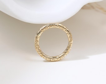 May include: A circular gold hoop earring featuring an intricate, embossed scrollwork pattern across its entire surface. The jewelry piece is designed with a hinged mechanism, allowing it to open and close securely for comfortable wear as a piercing.