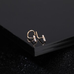 Peut inclure: Un bijou de nez en or rose avec une tige courb&eacute;e en forme de L et un motif d&eacute;licat orn&eacute; de deux petites pierres transparentes taille marquise. Le m&eacute;tal pr&eacute;sente une finition chaude et les pierres sont dispos&eacute;es en ligne sur la tige.