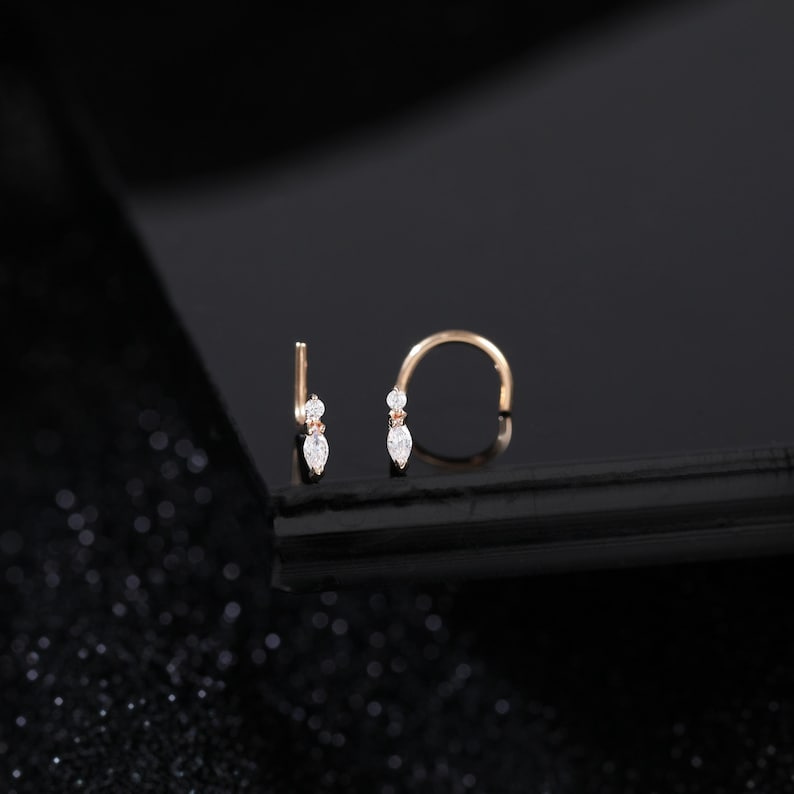 Peut inclure: Deux anneaux de nez en or rose pr&eacute;sentant un design d&eacute;licat avec une petite pierre ronde transparente plac&eacute;e au-dessus d'une pierre transparente taille marquise. Les bijoux sont fabriqu&eacute;s avec un fil m&eacute;tallique fin et raffin&eacute;.
