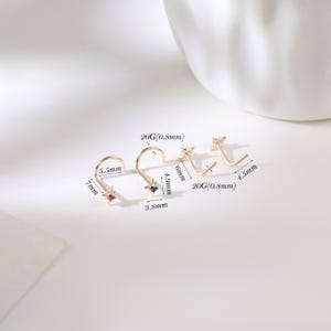 May include: Four gold-colored nose studs with star-shaped designs and gemstone accents. The studs vary in size, with measurements in millimeters and gauge (20G/0.8mm). One stud has a red gemstone, another a blue gemstone, and the others have clear gemstones.