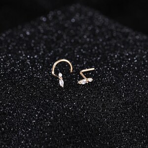 Peut inclure: Deux bijoux de nez dor&eacute;s dot&eacute;s d'une tige courb&eacute;e et d'une extr&eacute;mit&eacute; d&eacute;corative orn&eacute;e d'une petite pierre ronde transparente et d'une pierre transparente taille marquise. Les bijoux sont dispos&eacute;s c&ocirc;te &agrave; c&ocirc;te, r&eacute;v&eacute;lant le m&eacute;tal d&eacute;licat.