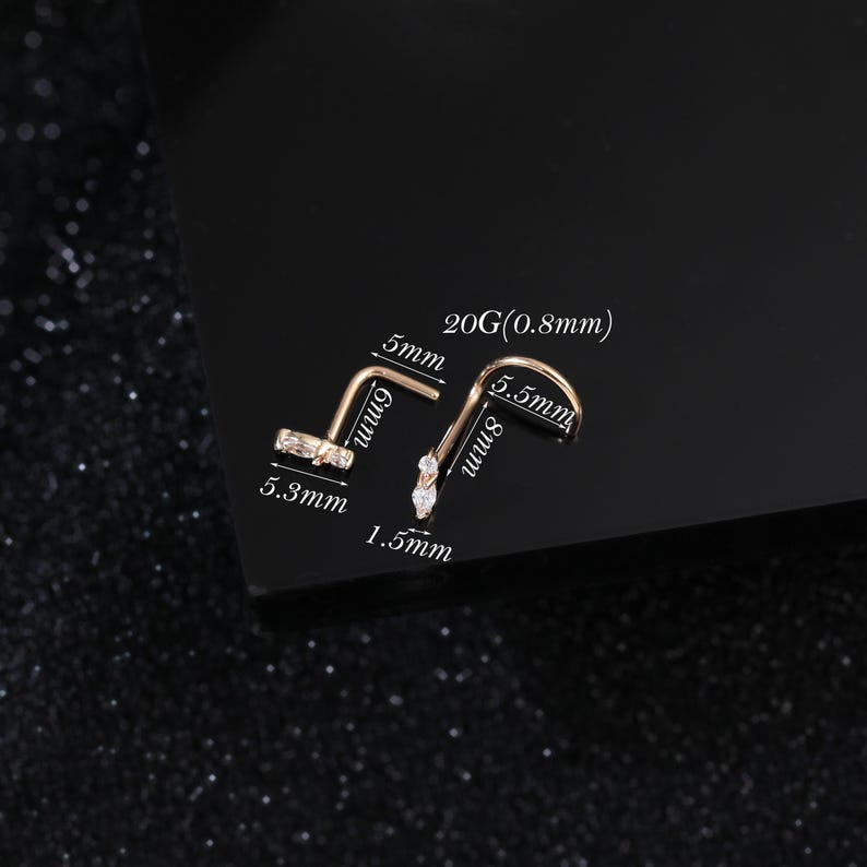 Peut inclure: Deux bijoux de nez dor&eacute;s avec des pierres transparentes. L'un est en forme de L avec des dimensions de 5mm par 6mm et un sertissage de 5,3mm. L'autre est courb&eacute; avec des dimensions de 5,5mm par 8mm, un sertissage de 1,5mm et un calibre 20G (0,8mm).