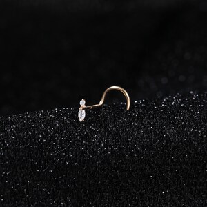 Peut inclure: Un piercing de nez en or rose avec une tige courb&eacute;e et une partie d&eacute;corative compos&eacute;e d'une petite pierre ronde transparente et d'une pierre transparente en forme de marquise dispos&eacute;es verticalement. Le m&eacute;tal a une finition chaude.