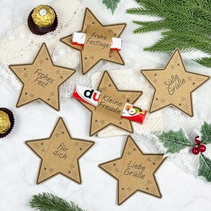 Può includere: Tag regalo a forma di stella marrone con decorazioni a stella e testo in tedesco. Alcuni tag contengono barrette di cioccolato. Il testo sui tag include "Frohes Fest", "Frohe Festtage", "für dich", "Kleine Freude", "Liebe Grüße" e "Süße Grüße".