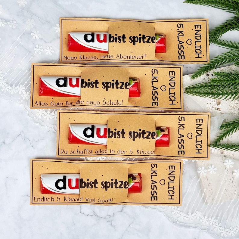 May include: Four chocolate bars wrapped in tan paper sleeves with black text. Each sleeve features the German phrase 'du bist spitze' and 'ENDLICH 5. KLASSE' with a heart icon. The individual messages include 'Neue Klasse, neue Abenteuer!', 'Alles Gute f&uuml;r die neue Schule!', 'Du schaffst alles in der 5. Klasse!', and 'Endlich 5. Klasse! Viel Spa&szlig;!'.