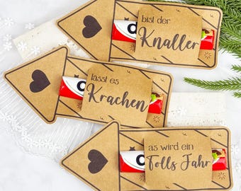 Puede incluir: Tarjetas de regalo de papel kraft con diseño de corazón y una barra de chocolate Kinder visible. Cada tarjeta tiene una frase alemana diferente, como "bist der Knaller" y "lässt es Krachen".