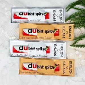 May include: Four chocolate bars wrapped in white and tan paper sleeves. Each sleeve features the text "du bist spitze" and "ENDLICH 5. KLASS" with a heart icon. The wrappers include additional German phrases like "Endlich 5. Klasse! Viel Spa&szlig;!"