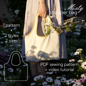 Op de afbeelding: Een crèmekleurige shopper met een gele rand, gevuld met witte bloemen, wordt door een persoon vastgehouden. De afbeelding bevat de tekst "Misty shopper bag" en details over een PDF naaipatroon met een video tutorial.